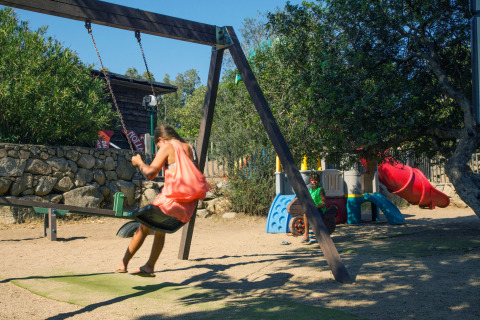Enfants jouant sur une aire de jeux avec balançoire et toboggan dans un parc de vacances glamping ensoleillé.