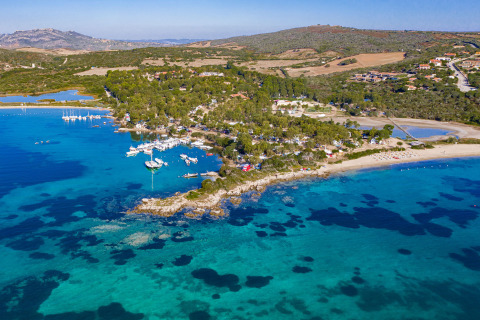 Aerial view of a holiday park with glamping options by the sea, surrounded by boats and lush greenery.