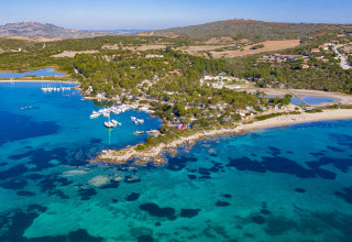 Vue aérienne d’un parc de vacances glamping près de la mer, avec bateaux et verdure luxuriante.