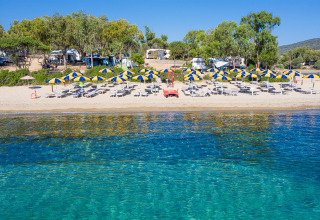 Beautiful holiday park beach with glamping, sunbeds and blue-yellow umbrellas on a sunny summer day.
