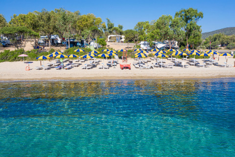 Beautiful holiday park beach with glamping, sunbeds and blue-yellow umbrellas on a sunny summer day.