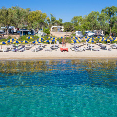 Playa de parque vacacional con glamping, tumbonas y sombrillas azul-amarillas en un día soleado.