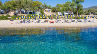 Playa de parque vacacional con glamping, tumbonas y sombrillas azul-amarillas en un día soleado.