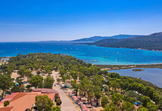 Vista aerea di un campeggio immerso nel verde con laguna blu e barche sulla splendida costa italiana.