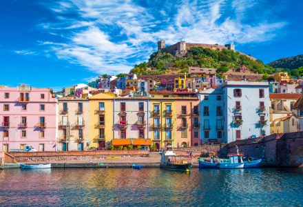 Casas coloridas junto al agua en una pintoresca ciudad cerca de Palau, Cerdeña, Italia, con castillo en la colina.