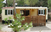 SunLodge Mobile Home Redwood en Camping Village Capo d'Orso, Italia, rodeado de árboles y flores blancas.