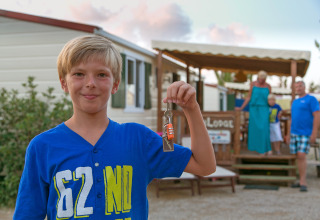 Jongen toont sleutels bij SunLodge Mobile Home Redwood op Camping Village Capo d'Orso, Italië.