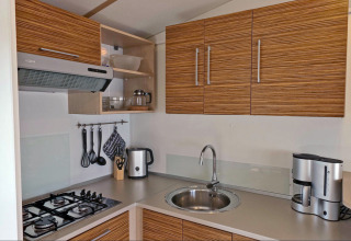 Moderne tekøkken i SunLodge Mobile Home Redwood på Camping Village Capo d'Orso, Italien, med træskabe og gaskomfur.