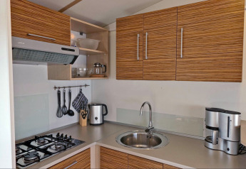 Moderne kitchenette in SunLodge Mobile Home Redwood op Camping Village Capo d'Orso, Italië, met houten kasten en apparatuur.
