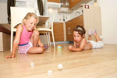 Twee kinderen spelen met dobbelstenen op de vloer van een moderne keuken in SunLodge Mobile Home Redwood, Italië.