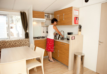 Mujer lavando platos en la cocina moderna de SunLodge Mobile Home Redwood en Camping Village Capo d'Orso, Italia.