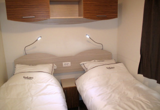 Twee enkele bedden met witte lakens en leeslampjes in SunLodge Mobile Home Redwood in Italië.