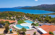 Vista aerea del Camping Village Capo d'Orso in Sardegna con piscina, alberi, edifici e mare azzurro sullo sfondo.