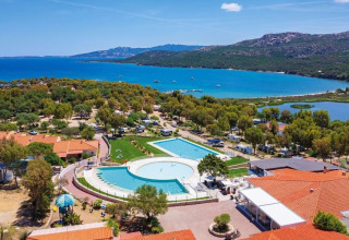 Aerial view of Camping Village Capo d'Orso in Sardinia, showing pool, greenery, buildings, and the sea.