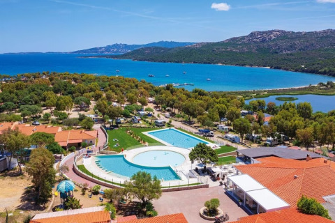 Vista aerea del Camping Village Capo d'Orso in Sardegna con piscina, alberi, edifici e mare azzurro sullo sfondo.