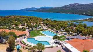 Vista aérea de Camping Village Capo d'Orso en Cerdeña, con piscina, árboles, edificios y el mar en el fondo.