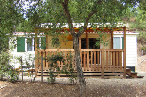 SunLodge Mobile Home Aspen at Camping Village Capo d'Orso, Italy, with a wooden deck and trees in front.
