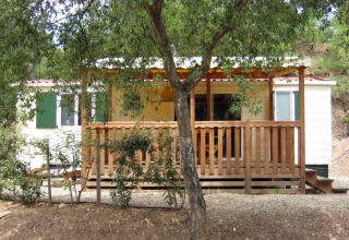 SunLodge Mobile Home Aspen en Camping Village Capo d'Orso, Italia, con terraza de madera y árboles delante.