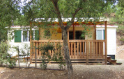 SunLodge Mobile Home Aspen en Camping Village Capo d'Orso, Italia, con terraza de madera y árboles delante.