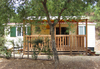 SunLodge Mobile Home Aspen at Camping Village Capo d'Orso, Italy, with a wooden deck and trees in front.