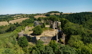 Vista aérea de un parque vacacional con glamping, mostrando ruinas de castillo rodeadas de bosques y campos.