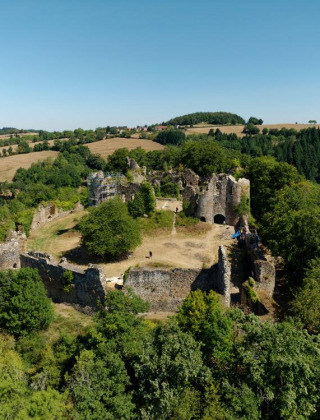 Vista aérea de un parque vacacional con glamping, mostrando ruinas de castillo rodeadas de bosques y campos.