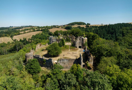 Aerial view of a holiday park offering glamping, featuring an ancient castle ruin surrounded by forests.