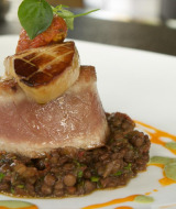 Plato gourmet con atún sellado, foie gras y lentejas servido en un plato blanco en parque de glamping.