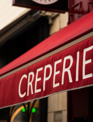Toldo rojo con la palabra 'CREPERIE' frente a un edificio, indicando una cafetería de crepas francesa.