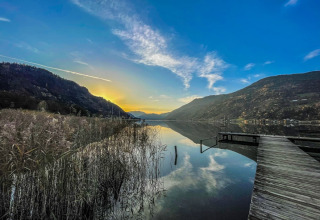 Sunset over a calm lake with mountains, reeds and a wooden pier, taken at a glamping holiday park.