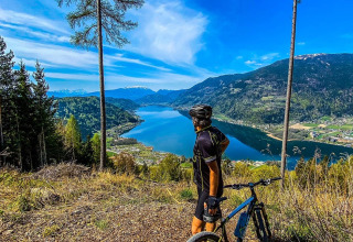 Een fietser bekijkt het meer en de bergen bij een vakantiepark met glampingaccommodaties.