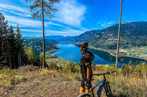 Un cycliste contemple un lac et des montagnes près d’un parc de vacances offrant du glamping.
