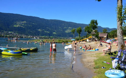 Familien genießen einen sonnigen Tag am See mit Bergen im Hintergrund in einem Glamping-Ferienpark.