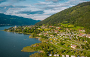 Aerial view of a holiday park with glamping by the lake, surrounded by green hills and small cottages.