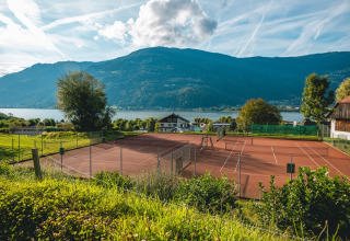 Tennisbane ved sø og bjerge i baggrunden, solrig dag i naturskønne omgivelser ved en feriepark.