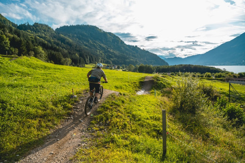 Fietser rijdt langs een pad in een vakantiepark met glamping, omgeven door heuvels en meerzicht.