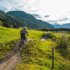 Ciclista recorre un sendero en un parque vacacional con glamping, rodeado de colinas y vistas al lago.