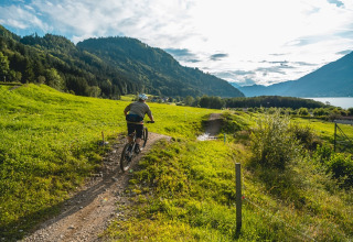 Cyclist rides along a scenic path in a holiday park with glamping, surrounded by hills and a lakeside view.