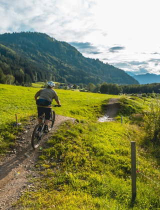 Ciclista recorre un sendero en un parque vacacional con glamping, rodeado de colinas y vistas al lago.