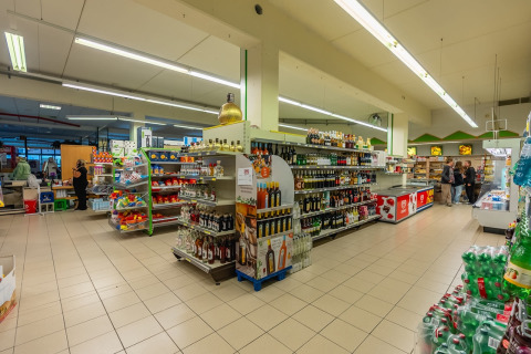 Afbeelding van supermarkt in vakantiepark met glampingaccommodaties, goedgevulde rekken en klanten.