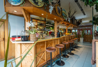 Gemütlicher Barbereich in einem Ferienpark mit Glamping, Holztresen, Hockern und rustikaler Dekoration.