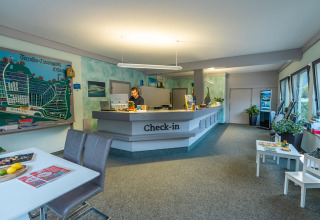 Mostrador de check-in en parque vacacional con glamping, empleado atendiendo, gran mapa del lugar.