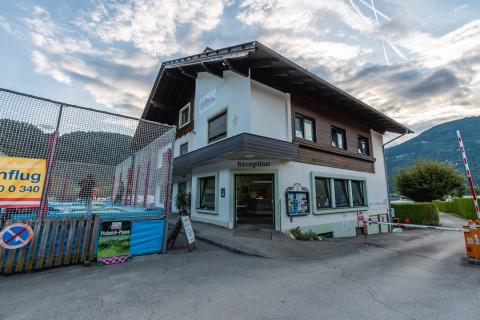 Buitenaanzicht van het receptiegebouw van het vakantiepark met bergen op de achtergrond, perfect voor glamping.