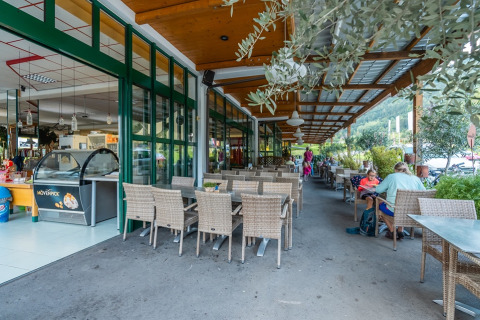 Buitenterras bij vakantieresort met glaspui, groene planten en gasten, perfect voor glamping.