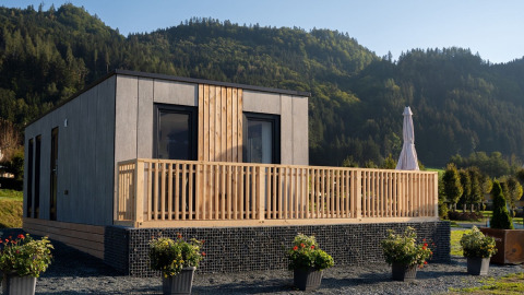 Moderna cabaña de glamping con terraza de madera y montañas al fondo en un parque vacacional.