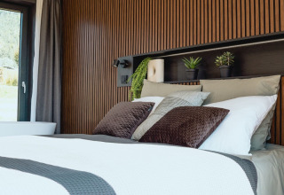 Modern glamping accommodation with a stylish bedroom, wood paneling, plants, and cozy bedding.