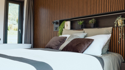 Modern glamping accommodation with a stylish bedroom, wood paneling, plants, and cozy bedding.
