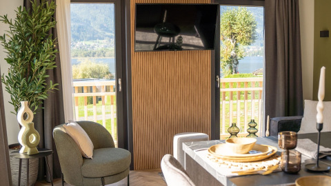 Modern glamping accommodation with stylish decor, dining table, and views of nature and a lake outside.