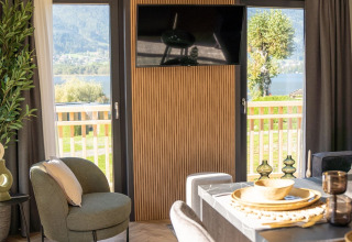 Hébergement de glamping moderne avec décoration élégante, table à manger et vue sur la nature et le lac.