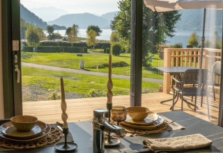 Udsigt fra et glamping-ophold med dækket spisebord, terrasse og bjergsø i baggrunden.